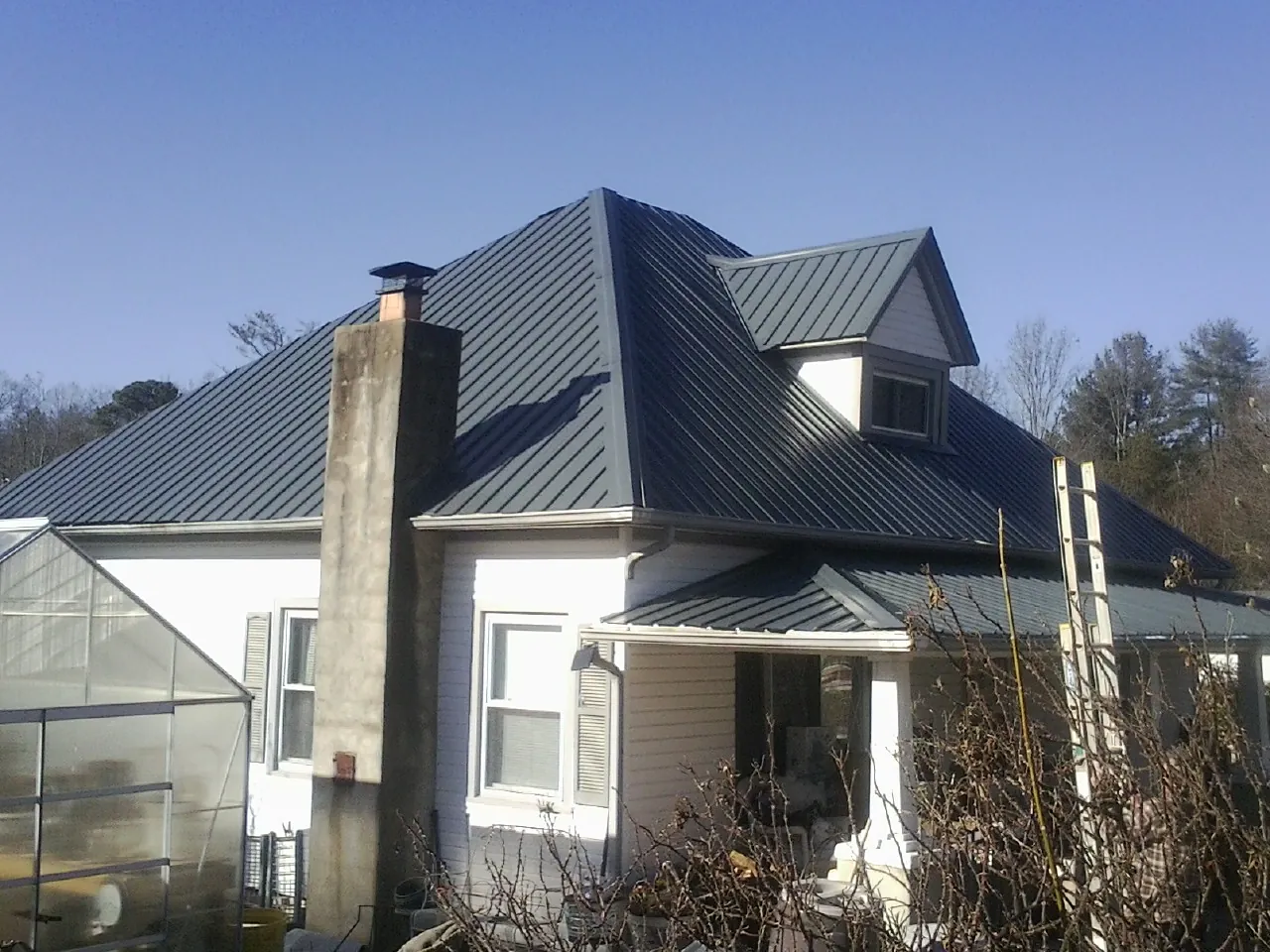 Dark blue standing seam metal roof on a white farmhouse with dormer — Slate & Tile Roof Repair by Roofing Brothers in Pony