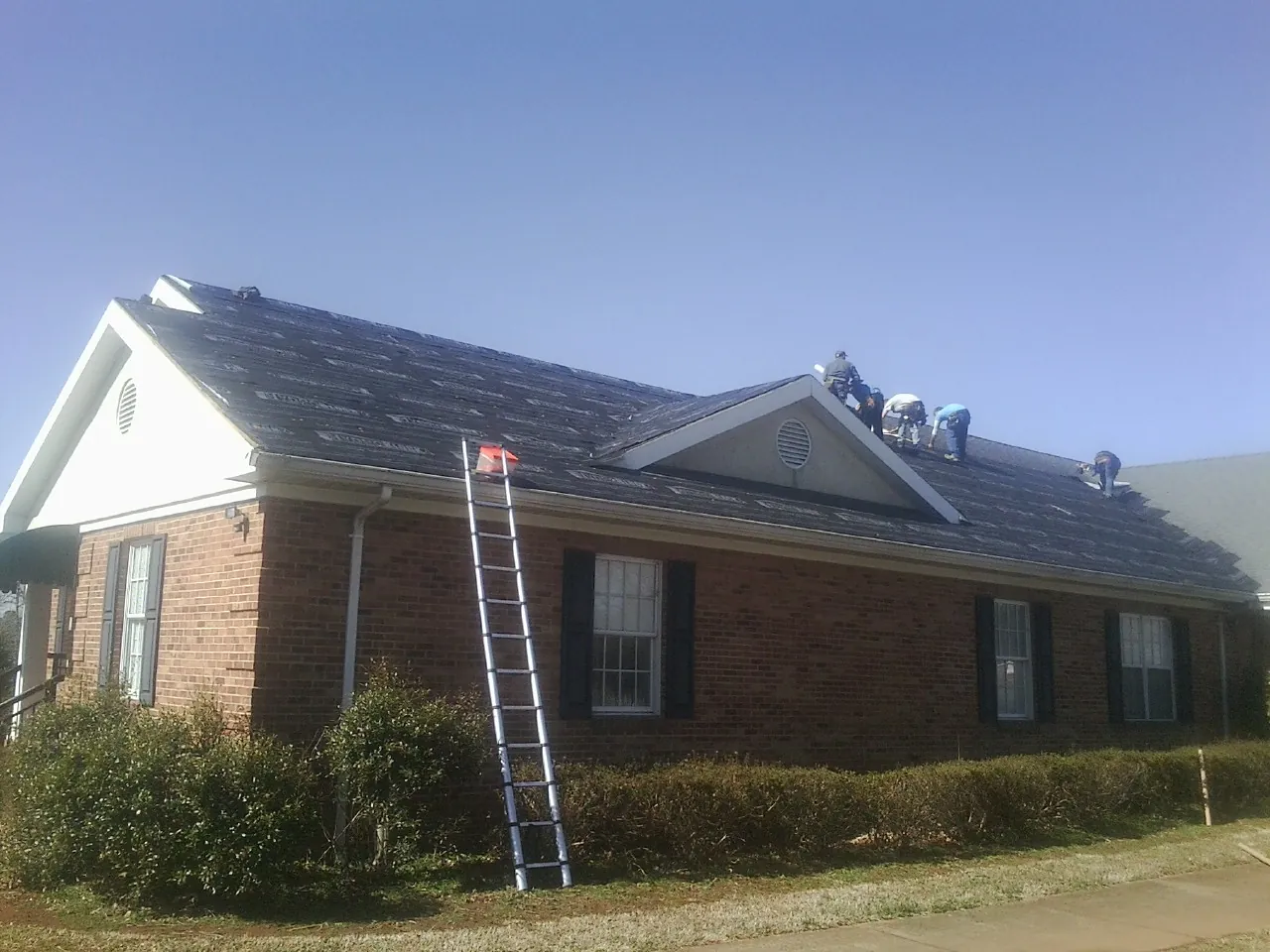 Crew tearing shingles off a brick ranch roof with a ladder set — Metal Roof Repair work by our crew in Pony