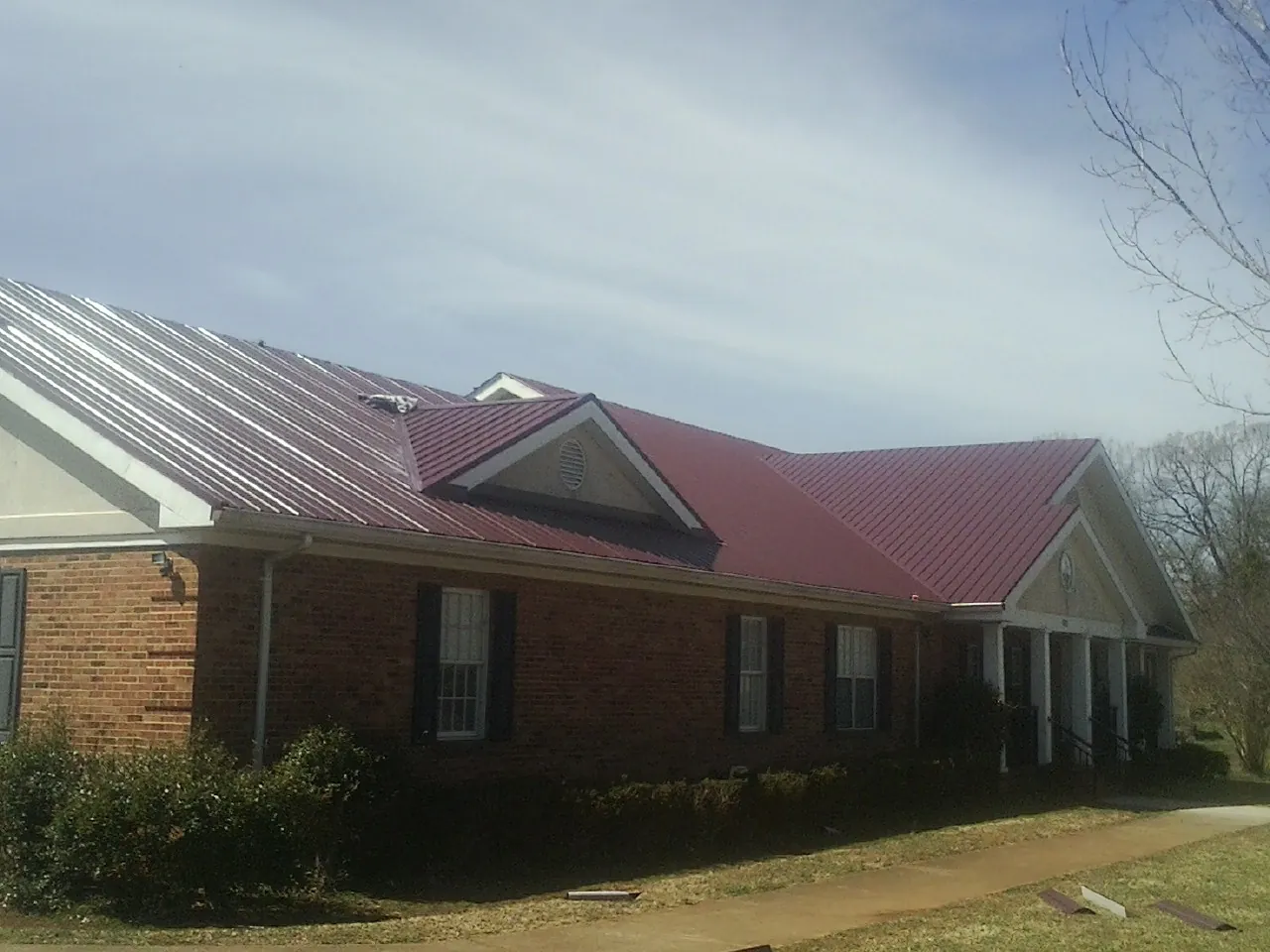 Red metal roof with gabled entries on a long brick building, from a Hail Damage Roof Repair job in Pony