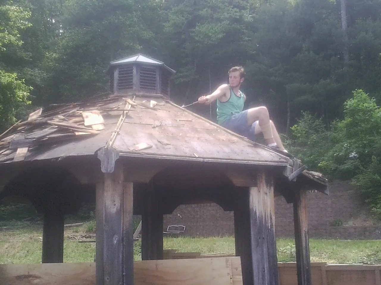 Tearing the old roof off a wooden gazebo before new shakes in Pony