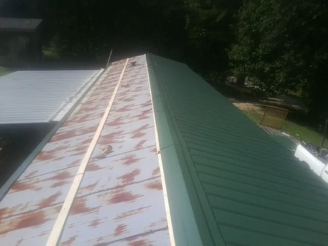 Old rusted panels beside newly installed green metal roofing — Wind Damage Roof Repair by Roofing Brothers in Pony