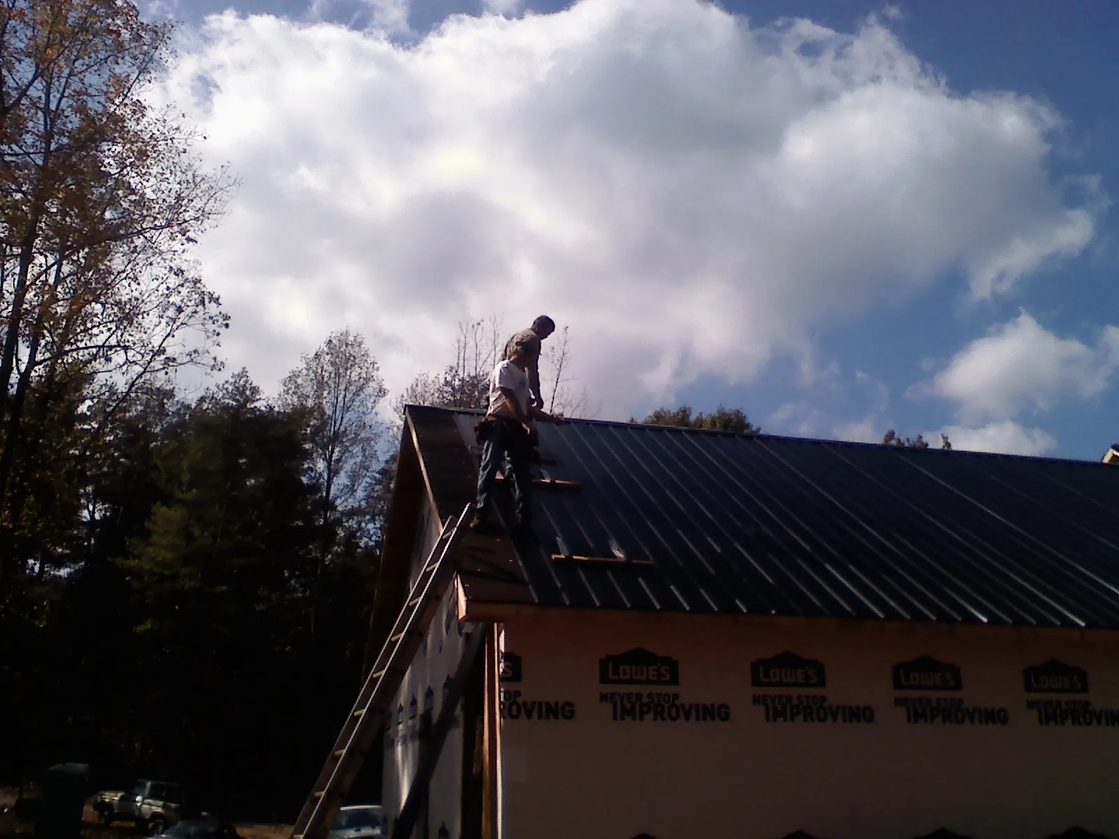 Roofer fastening dark metal panels high against a cloudy sky, from a Roof Inspection job in Pony